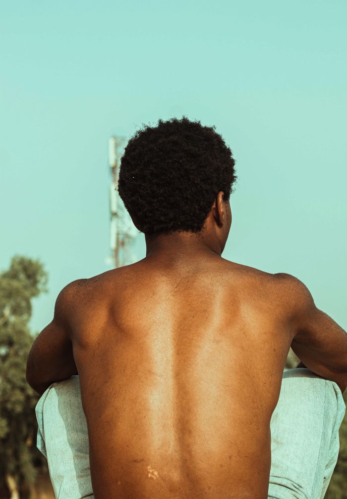 A shirtless man sitting outdoors on a bright day showcasing leisure and freedom.