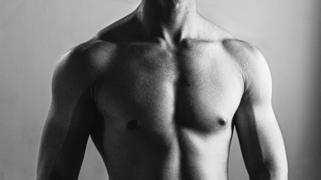 Grayscale photo highlighting muscular physique and masculinity of a shirtless man.